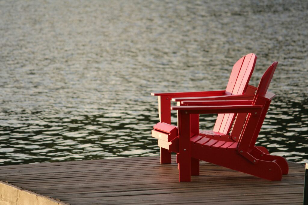 Two red Adirondack chairs on a wooden dock overlooking peaceful waters, ideal for relaxation.